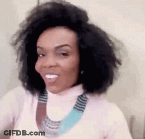 A Woman With Curly Hair Is Wearing A Pink Turtleneck And A Blue Necklace . GIF