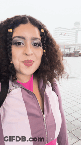 A Woman With Curly Hair Is Wearing A Purple And White Striped Jacket GIF