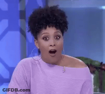 A Woman With Curly Hair Is Wearing A Purple Sweater And Hoop Earrings . GIF
