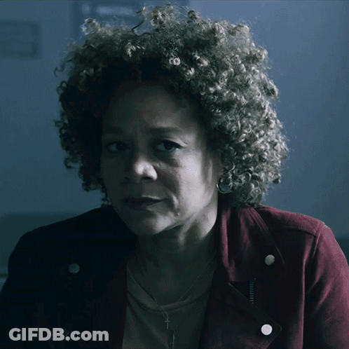 A Woman With Curly Hair Is Wearing A Red Jacket And Earrings GIF