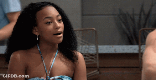 A Woman With Curly Hair Is Wearing A Strapless Top And Earrings GIF