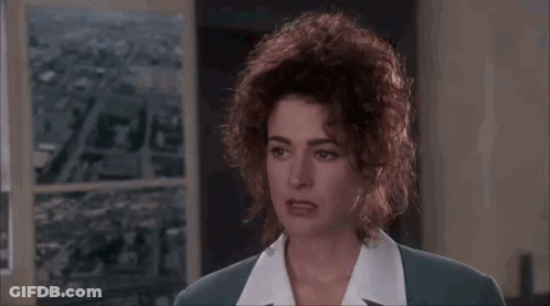 A Woman With Curly Hair Is Wearing A Suit And A White Shirt And Making A Funny Face . GIF