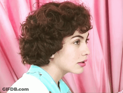 A Woman With Curly Hair Is Wearing A White Shirt And A Blue Scarf GIF