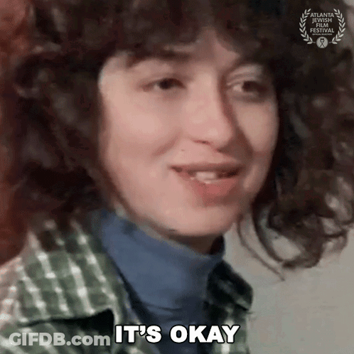 Curly Haired Woman Saying It's Okay In Plaid Shirt GIF