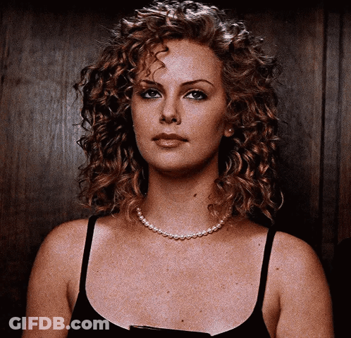 A Woman With Curly Hair Wearing A Black Tank Top And A Pearl Necklace GIF