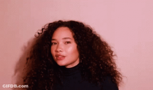A Woman With Curly Hair Wearing A Black Turtleneck Sweater GIF