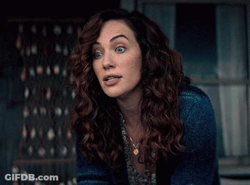 A Woman With Curly Hair Wearing A Blue Sweater And A Necklace GIF