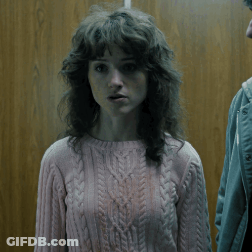 A Woman With Curly Hair Wearing A Pink Sweater Looks Surprised GIF