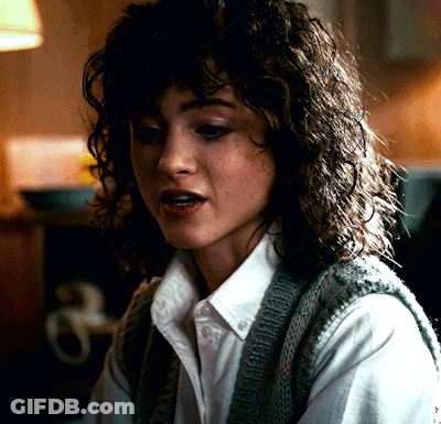 A Woman With Curly Hair Wearing A White Shirt And Sweater Vest GIF