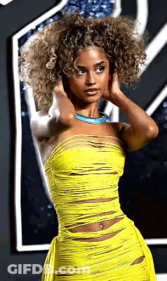 A Woman With Curly Hair Wearing A Yellow Dress And A Blue Necklace . GIF