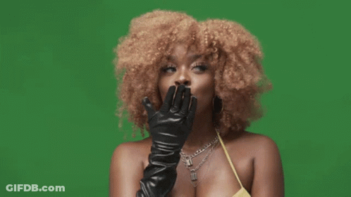 A Woman With Curly Hair Wearing A Yellow Top And Black Leather Gloves GIF