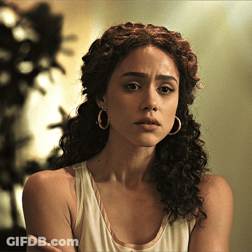 A Woman With Curly Hair Wears Hoop Earrings And A White Tank Top GIF