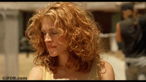 A Woman With Curly Red Hair Is Looking Down At Something . GIF