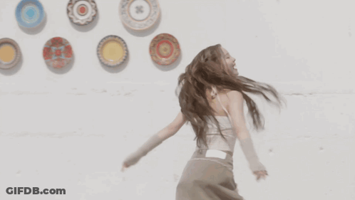A Woman With Dreadlocks Is Dancing In Front Of Plates On A Wall GIF
