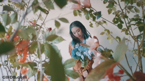 A Woman With Dreadlocks Is Holding A Bouquet Of Flowers GIF