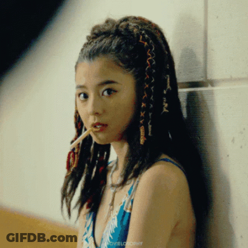 A Woman With Dreadlocks Is Leaning Against A Wall And Smoking GIF