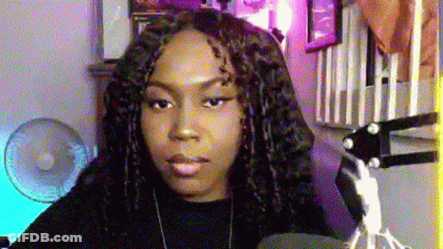 A Woman With Dreadlocks Is Sitting In Front Of A Microphone In A Room With A Fan . GIF