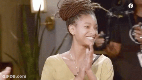 A Woman With Dreadlocks Is Smiling And Clapping Her Hands While Wearing A Yellow Shirt . GIF