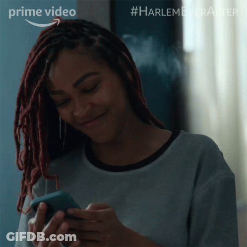 A Woman With Dreadlocks Is Smiling While Looking At Her Phone And The Words Prime Video Are Above Her GIF