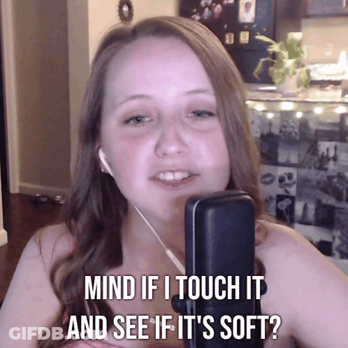 A Woman With Ear Buds Is Talking Into A Microphone With The Words Mind If I Touch It And See If It 'S Soft GIF