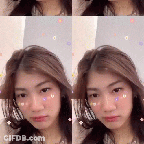 A Woman With Flowers On Her Face Is Looking At The Camera GIF