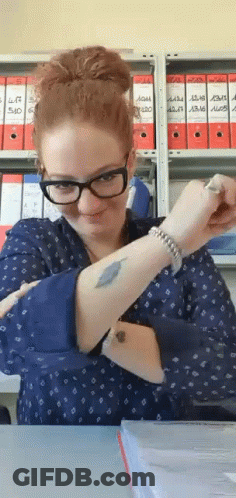 A Woman With Glasses And A Tattoo On Her Arm Is Sitting At A Table . GIF