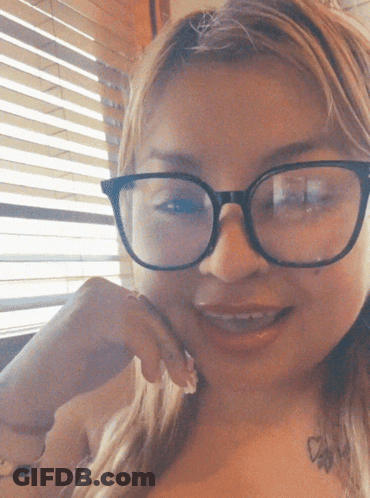 A Woman With Glasses And A Tattoo On Her Chest Smiles GIF