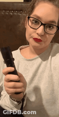 A Woman With Glasses And Red Lipstick Is Holding A Flashlight GIF
