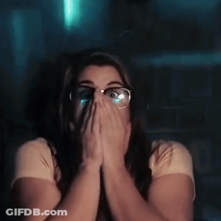 A Woman With Glasses Is Covering Her Face With Her Hands While Watching A Movie . GIF