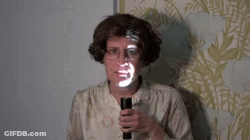 A Woman With Glasses Is Holding A Flashlight With A Face Projected On It GIF