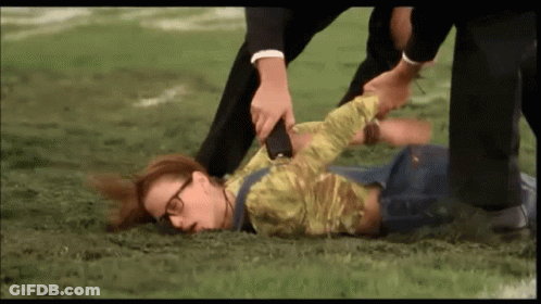 A Woman With Glasses Is Laying On The Ground While A Man Holds Her Arm GIF