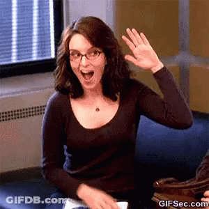 A Woman With Glasses Is Sitting On A Couch And Waving Her Hand . GIF
