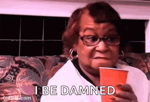 A Woman With Glasses Is Sitting On A Couch Holding A Red Cup And Saying `` I Be Damned '' . GIF