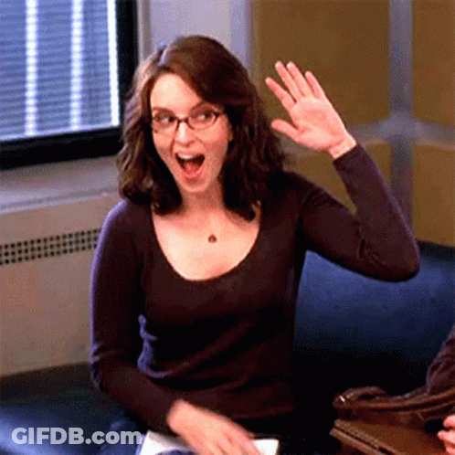 A Woman With Glasses Is Sitting On A Couch Waving Her Hand GIF