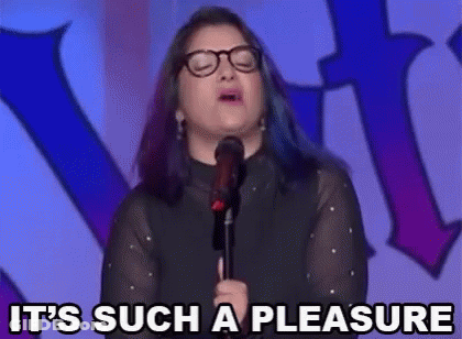 A Woman With Glasses Is Standing In Front Of A Microphone And Saying It 'S Such A Pleasure . GIF