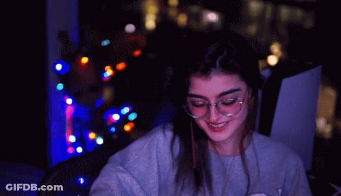 A Woman With Glasses Says Group Hug In A Dark Room GIF
