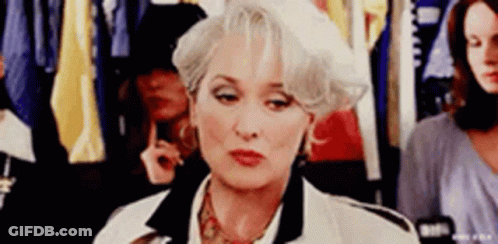 A Woman With Gray Hair And A White Hat Is Sitting In A Dressing Room . GIF