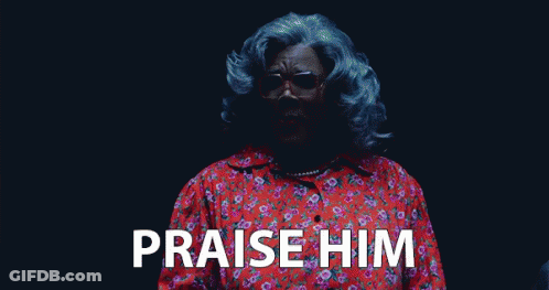 A Woman With Gray Hair And Glasses Is Standing In A Dark Room And Saying Praise Him . GIF