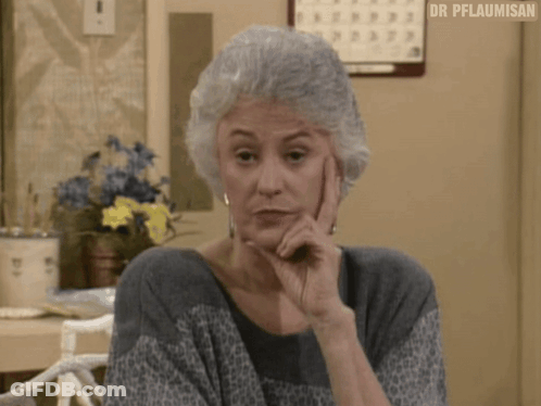 A Woman With Gray Hair Is Sitting At A Table With Her Hand On Her Chin And A Calendar On The Wall Behind Her . GIF