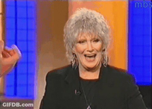 A Woman With Gray Hair Is Smiling In Front Of A Blue Wall With Mbs Written On It GIF