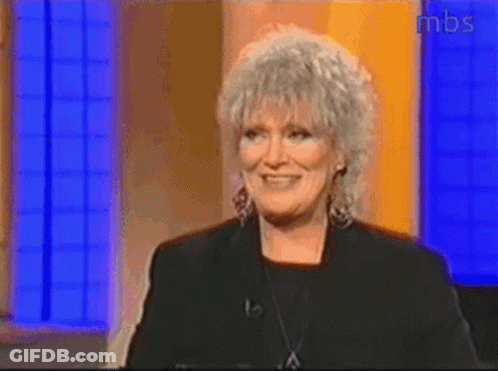 A Woman With Gray Hair Is Smiling In Front Of A Mbs Sign GIF