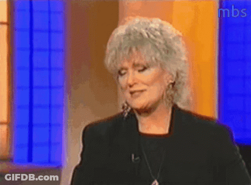 A Woman With Gray Hair Is Standing In Front Of A Blue Wall With Mbs Written On The Bottom GIF