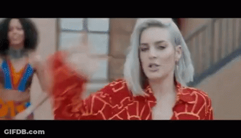 A Woman With Gray Hair Is Wearing A Red Shirt And Dancing On A Staircase . GIF