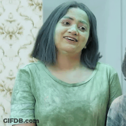 A Woman With Green Hair And A Green Shirt Is Smiling And Looking At The Camera . GIF