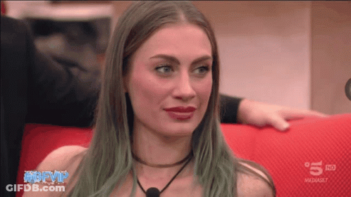 A Woman With Green Hair Is Sitting On A Red Couch In Front Of A 5 Hd Sign GIF