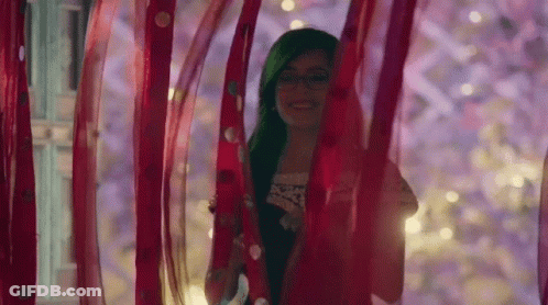 A Woman With Green Hair Is Standing Behind A Red Curtain . GIF