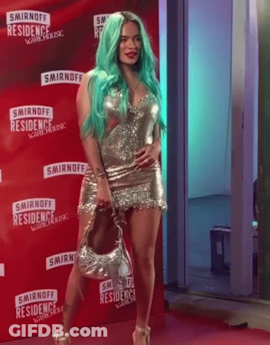 A Woman With Green Hair Is Standing On A Red Carpet In Front Of A Smirnoff Sign GIF