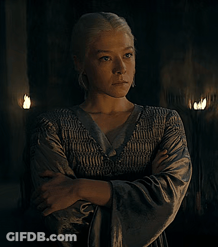 A Woman With Her Arms Crossed And Her Eyes Closed Stands In A Dark Room GIF