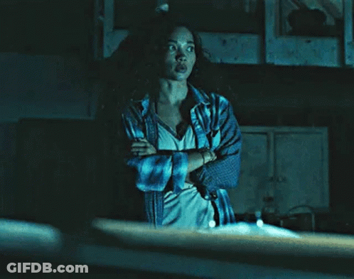 A Woman With Her Arms Crossed Is Standing In A Dark Room . GIF