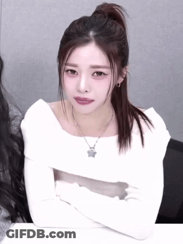 A Woman With Her Arms Crossed Wearing A White Top And A Necklace With A Star On It GIF